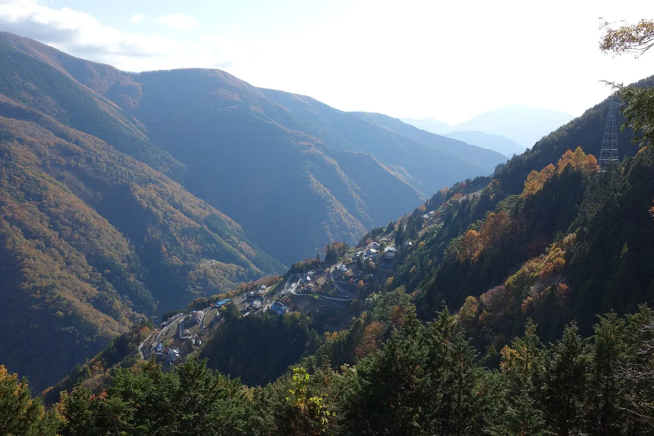 山あいの急な斜面に家と畑が張りつく、紅葉の下栗の里を見下ろす