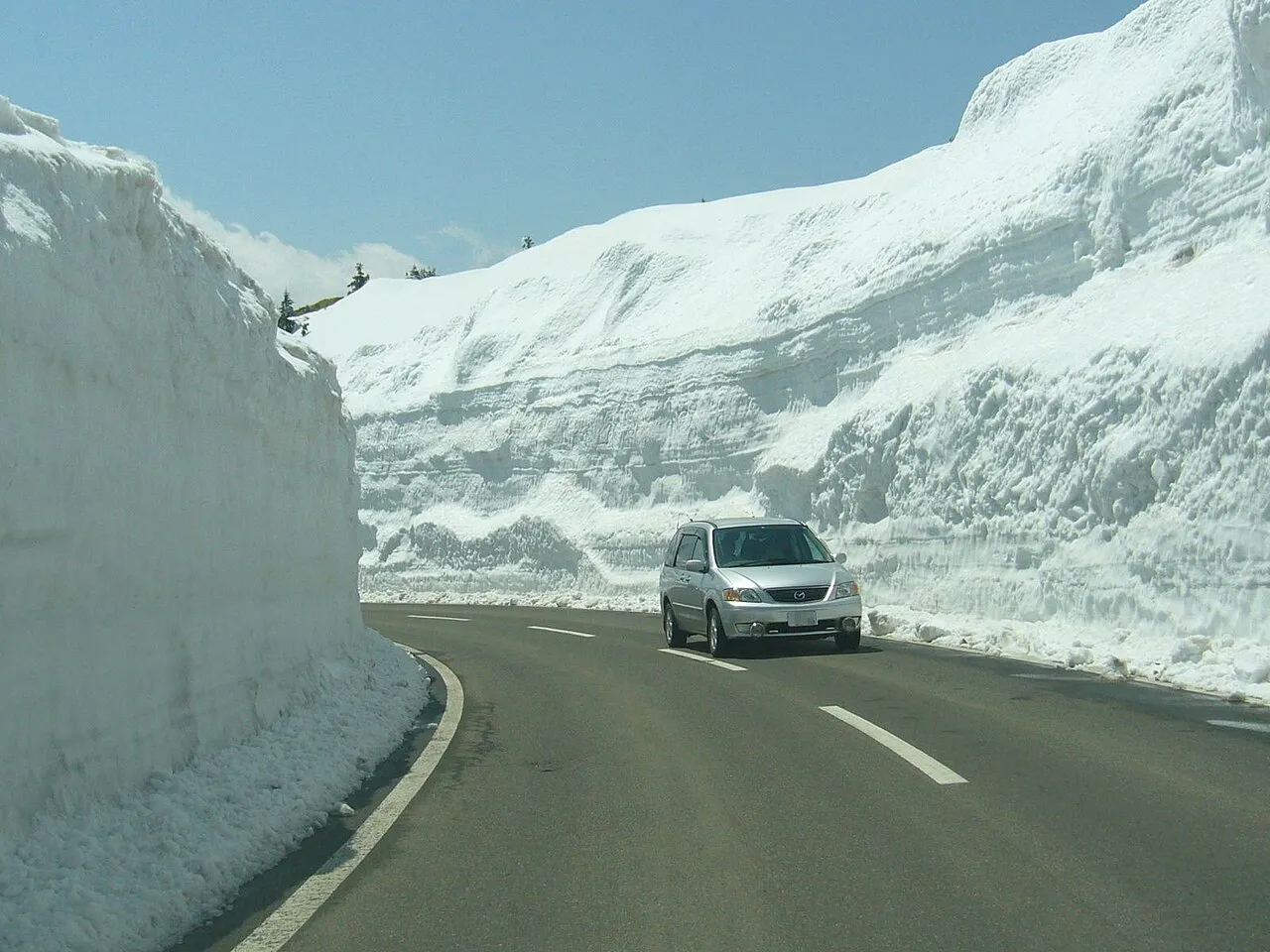 Route 292 at Shibu Pass in spring, with tall walls of snow on both sides and a car driving through