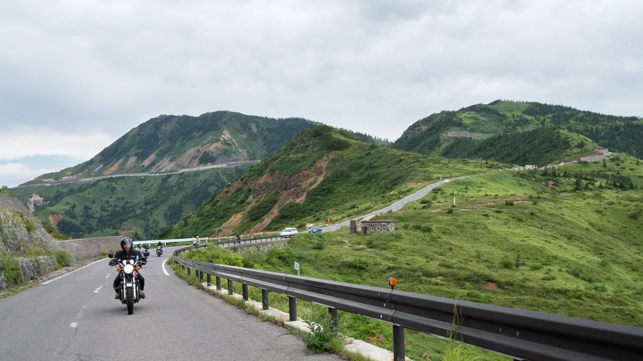 緑の山の斜面を縫う国道292号と、走るオートバイ